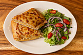 Top view of appetizing baked chapatas with mixed salad of tomato onions and green lettuce served on white marble plate on wooden surface in light