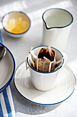 Eine heitere Szene mit einer Tropfkaffeetasse mit Filter, die auf einem Teller neben einem silbernen Krug und einer Schale mit Honig steht, getaucht in sanftes Morgenlicht
