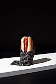 Appetizing bun with sausage and ketchup served table mat over white wooden board against black background in studio
