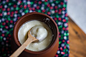Hohe Ansicht einer traditionellen Portion georgischen sauren Joghurts, bekannt als Matsoni, in einem Tongefäß mit Holzlöffel auf einer bunten Serviette vor einem unscharfen Hintergrund