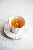 High angle of glass of floral tea with fresh herbs served on ceramic plate against gray background