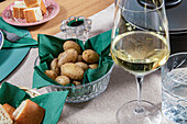 A sophisticated table setting featuring a glass of white wine, fresh bread, and a bowl of baked potatoes ready for a dinner party.