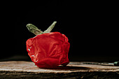 A red plastic bag sculpted to resemble a vegetable or fruit on a wooden surface against a black background