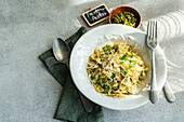 A plate of Farfalle pasta with pesto and grated cheese garnished with fresh herbs, alongside silverware and a label.