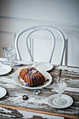 Leckerer süßer Schokoladenkuchen mit frischen Blumen auf einem weißen Keramikteller auf einem Holztisch mit Glaswaren