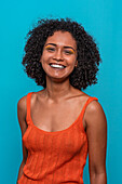 Smiling African American female model in casual clothes with dark curly hair looking at camera against blue background