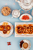 A top-down view of an elegant tea time spread featuring snacks, a tea pot, and a cup filled with tea on a blue background.