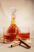 Glasses of whiskey placed on table near decanter and cinnamon sticks against white background