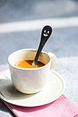 Cup of spicy espresso with spoon placed on napkin against gray table
