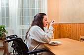 Content woman in a wheelchair enjoys a homemade meal at a dining table, exemplifying accessibility at home
