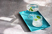 Two stylish cocktail glasses on a blue textured serving tray, adorned with mint leaves, set against a soft shadowy background