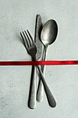 Top view of vintage cutlery set placed on gray surface with red ribbon in light kitchen