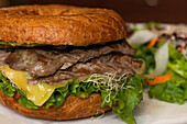 Closeup of tasty burger with whole beef cheese fresh lettuce and vegetables carrot sprouts placed on plate against blurred background in kitchen