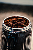 Top view of finely ground coffee filling a ribbed glass jar, highlighting its rich texture and depth, placed on a mottled background