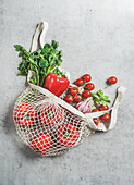 Draufsicht auf verschiedene Gemüse und Kräuter in einer wiederverwendbaren, plastikfreien Einkaufstasche am grauen Betonküchentisch