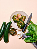 Grüne Tomaten mit anderen Gemüsesorten wie Zucchini und Bok Choy in hellem Sonnenlicht, flachgelegter Teller mit Messer und Kopierbereich auf beigem Hintergrund