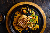 Top view of traditional Ecuadorian dish appetizing grilled fish steak garnished with mussels herbs and yellow sauce served on black plate