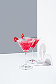 Glasses filled with red pomegranate cocktails served with pomegranate seeds against a gray and white backdrop, casting shadows