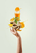Women hand holding balancing ginger and orange immunity boosting drink with splashing and ingredients at light background. Creative healthy lifestyle. Levitation food . Front view