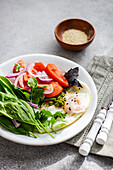 Fresh keto breakfast featuring poached eggs, spinach, tomatoes, and herbs on a white plate, ideal for a low-carb diet.