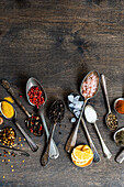 Top view of variety of colorful spices and seeds neatly arranged in spoons on a rustic wooden background for culinary concepts.