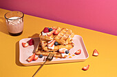 From above tasty sweet waffles topped with berries fruits sauce and cream served on pink tray on colorful table background near glass with hot milk beverage in light kitchen