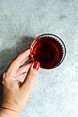 Top view of cropped unrecognizable hands of woman holding transparent glass of traditional saperavi Georgian red wine served in clean concrete gray background table