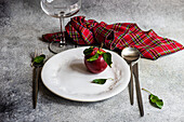 High angle of ripe red apple in plate placed between knife,spoon and fork with cloth and empty glass on gray surface