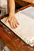 Hand eines nicht erkennbaren männlichen Bäckers, der beim Backen von leckerem Gebäck in einer Backstube durch Drücken der Ränder Muster auf gefüllten rohen Teig zeichnet