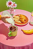 Unrecognizable person pouring fresh milk into cup of hot aromatic coffee placed on table with delicious croissants and banana decorated by flowers in vase