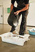 Unrecognizable male worker in overall pouring ice out of large bag in plastic container with fish in Spain