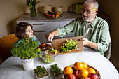 High angle view of elderly grandfather wearing eyeglasses and putting lettuce in bowl while making salad with granddaughter at home