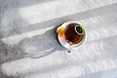 Top view of transparent cup of hot tea with a slice of lemon on a saucer and a green tea infuser hanging on the side