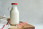 Raw cow milk in vintage closed bottle on cutting board near drinking straws and napkin against gray surface