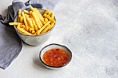 High angle of ceramic bowls with French fries and sour sweet sauce placed on white surface near napkin