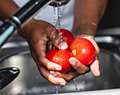 Cropped unrecognizable African American male washing fresh bell pepper in sink with water stream while cooking healthy salad in kitchen
