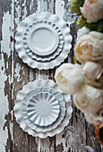 Top view of various white decorative ceramic plates placed on shabby lumber table near blooming flowers in vase