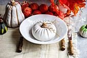 High angle of autumnal table setting with white pumpkin on plate placed on table near cutlery, glasses and red onions and leaves
