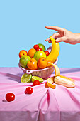 Anonymous person taking a banana of plastic drying rack with fresh fruit on a table with a pink tablecloth