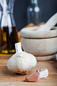 A close-up image featuring a whole garlic bulb and individual cloves with a mortar and kitchen utensils in the blurry background.