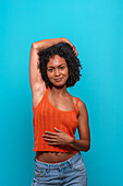 Smiling slim African American female model in casual clothes with dark curly hair looking at camera against blue background