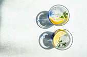 Top view of Summer cocktails with lemon vodka, slices of lemon and wild mint leaves served with ice placed on white table
