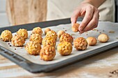 Crop anonymous person placing sweet panellets on tray on wooden table against blurred background