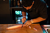 A skilled sushi chef meticulously prepares fresh fish with precision, showcasing the art of sushi-making.