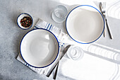 Modern dinnerware arrangement on a marble surface, including white plates with blue trim, silverware, and a striped napkin, creating an elegant table setting.