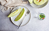 From above slices of green melon placed in a ceramic dish with a lemonade on concrete background