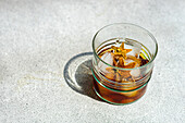 High angle of glass of whiskey with ice and orange peel placed on gray background