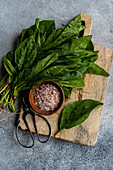 Draufsicht auf ein Bündel frischer Spinatblätter auf einem rustikalen Holzbrett, begleitet von aromatischen Gewürzen in einer Schüssel, die die Zubereitung eines gesunden Salats symbolisiert