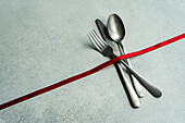 High angle of vintage cutlery set placed on gray surface with red ribbon in light kitchen