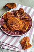 High angle of slices of dried apples served on ceramic plate on striped napkin against blurred gray background